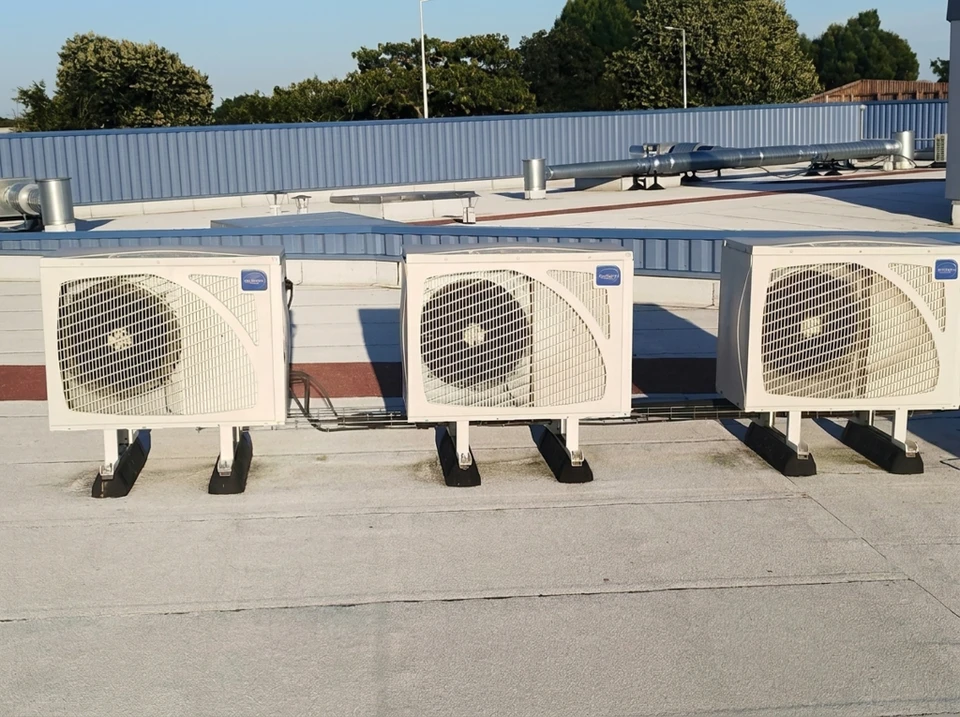 Technicien tenant un manifold de climatisation avec deux manomètres à cadran bleu et rouge, connecté par des flexibles colorés devant une unité extérieure de climatisation résidentielle